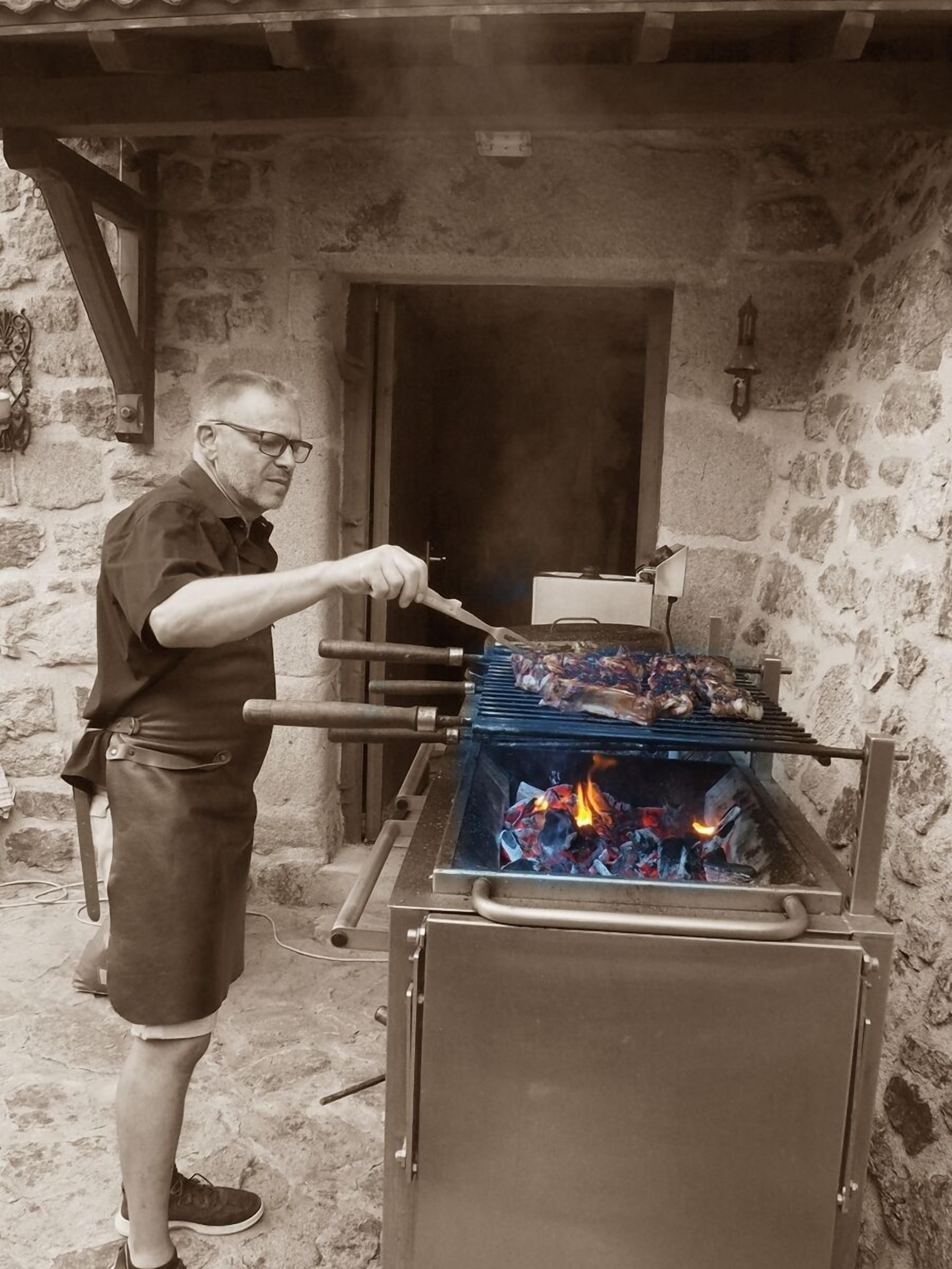 A man grilling food on an outdoor grill with a stone wall background.