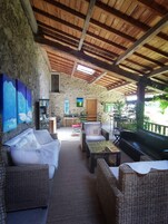 Un espacio al aire libre acogedor con mobiliario de mimbre, pared de piedra y techo de madera.