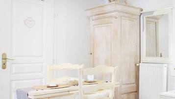 A room with a wooden ceiling, a white wardrobe, a white chair, a small table, and a fluffy rug.