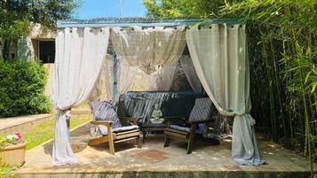 Un espace extérieur aménagé, abrité et doté d’une table et de chaises, entouré de verdure et délimité par une clôture en bambou.