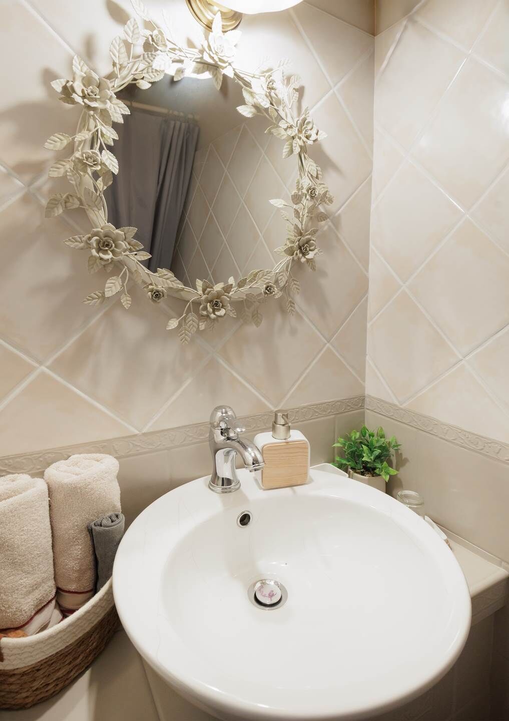 Une salle de bain avec un lavabo blanc, un miroir orné d’un cadre floral et un porte-serviettes avec des serviettes.