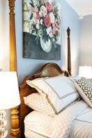 Un dormitorio con estructura de cama de madera, un cuadro floral en la pared y una lámpara de noche.