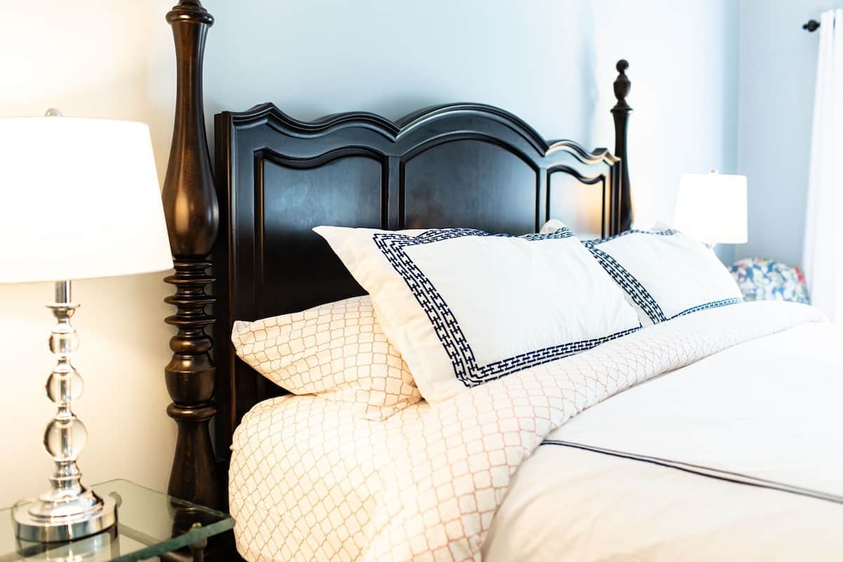Una cama bien hecha con ropa de cama estampada, un cabecero de madera oscura y dos lámparas de noche sobre mesitas de cristal.