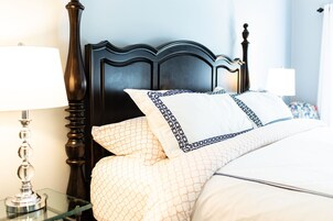 Una cama bien hecha con ropa de cama estampada, un cabecero de madera oscura y dos lámparas de noche sobre mesitas de cristal.