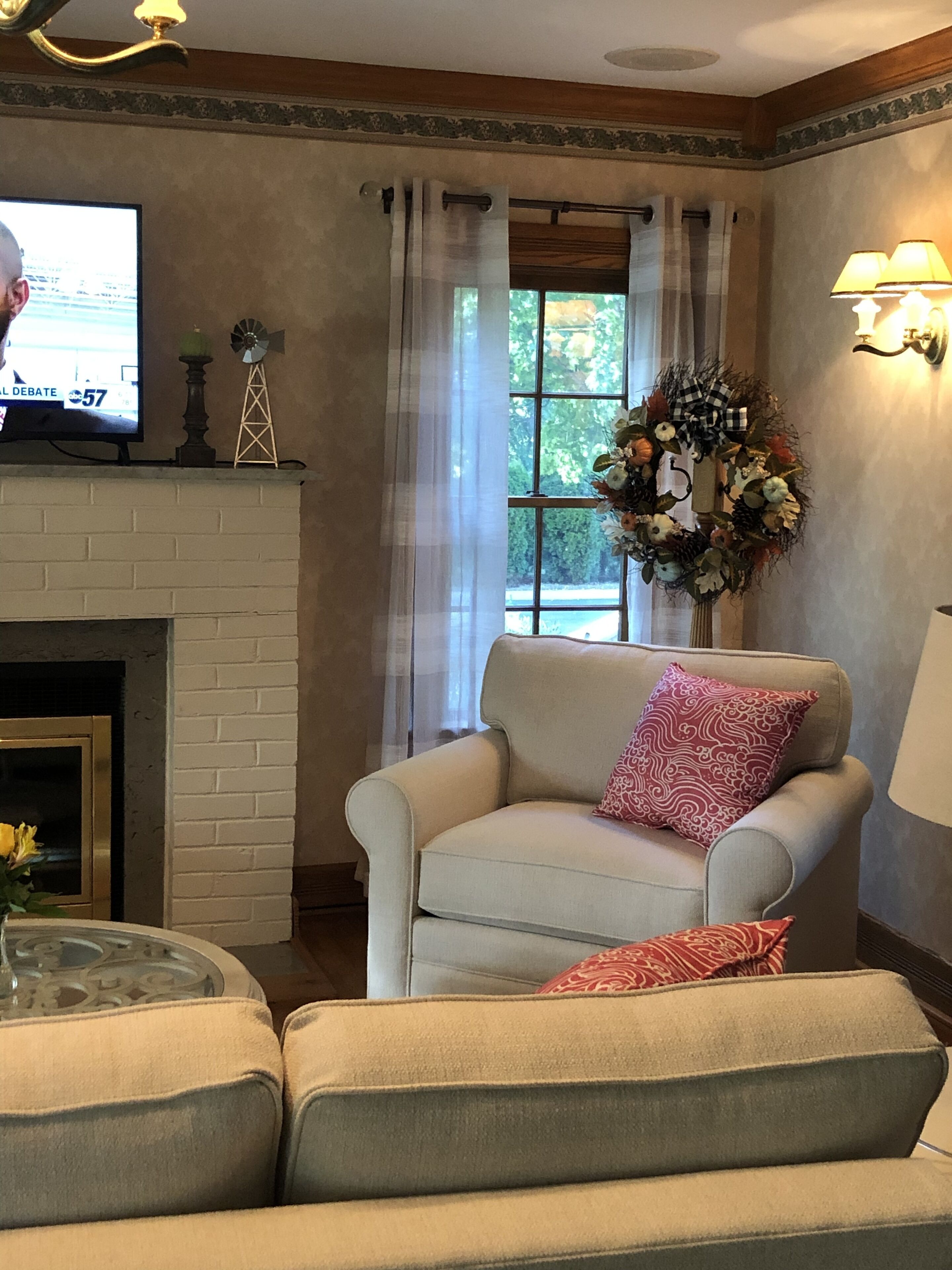 Un salon avec une cheminée, un téléviseur, une fenêtre avec des rideaux et un arrangement floral.