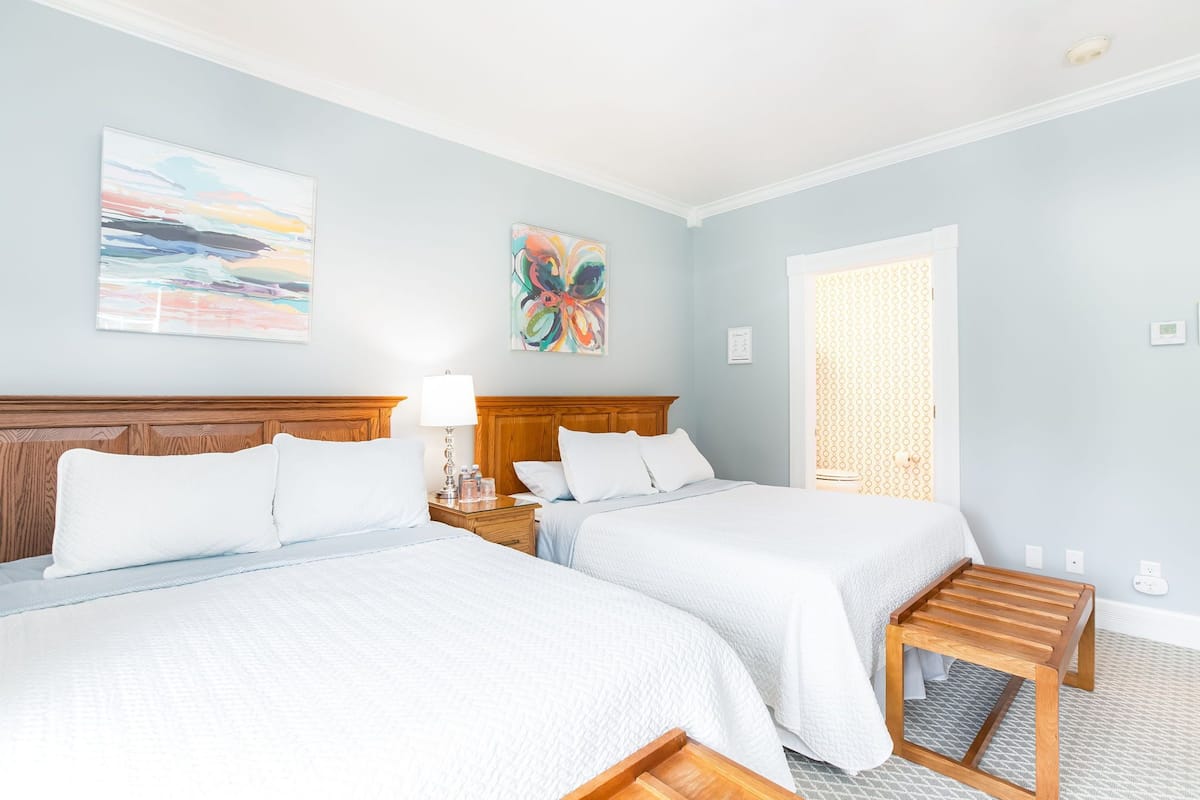Habitación de hotel con dos camas, cabecero de madera, mesita de noche con lámpara y decoración abstracta en la pared.