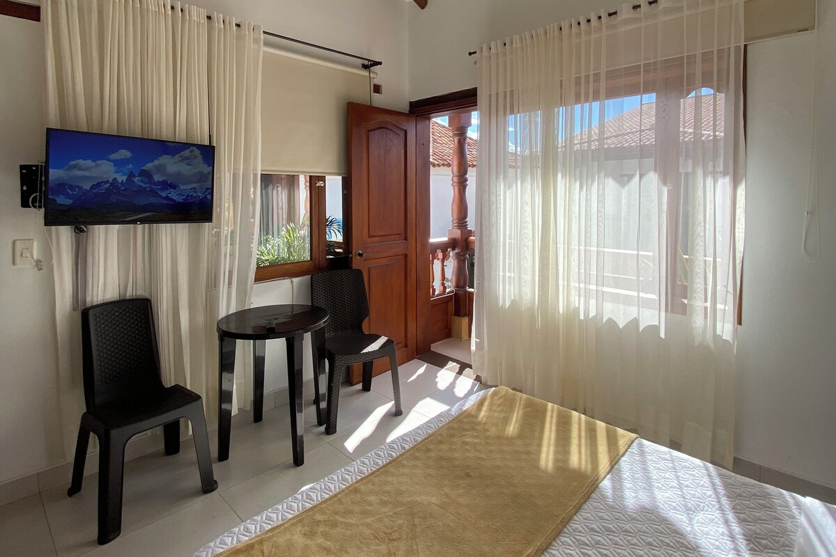 Habitación de hotel con cama, televisor, escritorio y una silla. Se ve una puerta que da a un área exterior.