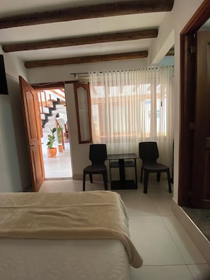 A hotel room with a bed, two chairs, a table, and a staircase leading to an outdoor area.