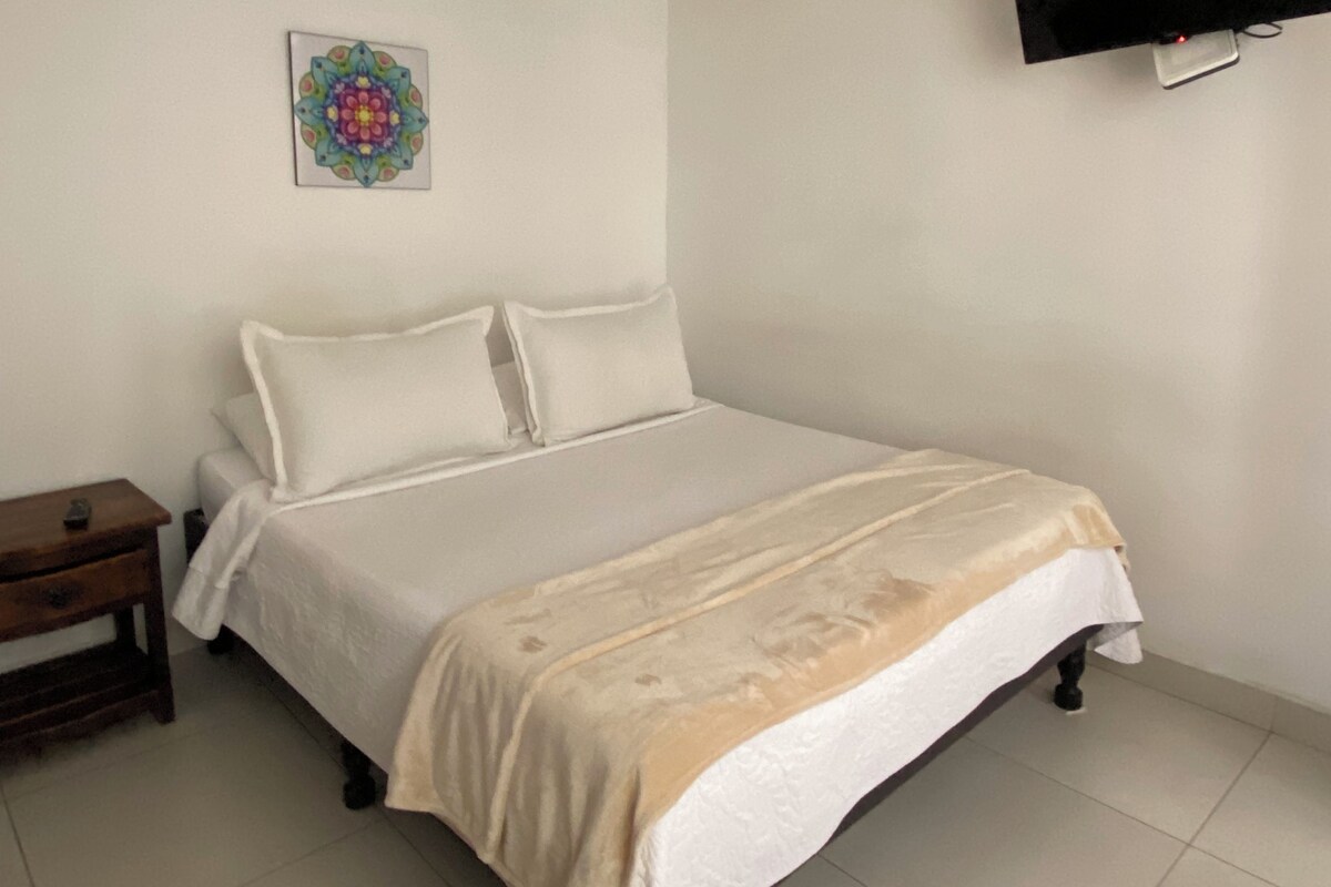 Un dormitorio con cama, una mesita de noche, televisor montado en la pared y un adorno mural.
