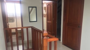 A wooden staircase with a handrail, a large wooden door, and a mirror on the wall. - Hospedaje Villa Monica (Villa de Leyva)
