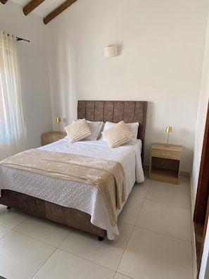 A bedroom with a bed, two bedside tables, a nightstand, and a wall-mounted lamp.