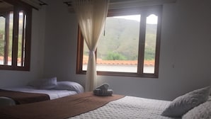 A room with two beds, a window with curtains, and a view of a hilly landscape. - Hospedaje Villa Monica (Villa de Leyva)