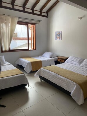 Habitación con dos camas individuales, una mesita de noche de madera, una ventana con cortinas y un cuadro colgado en la pared.