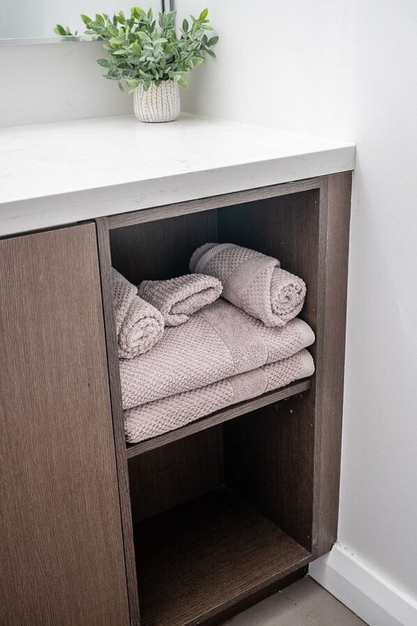 A bathroom with a white countertop, a potted plant, and neatly folded towels. - Charming Yorkville Condos (Toronto)