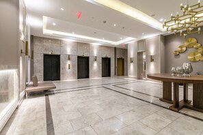 A spacious lobby with a marble floor, a round wooden table with glassware, and a modern chandelier. - Charming Yorkville Condos (Toronto)