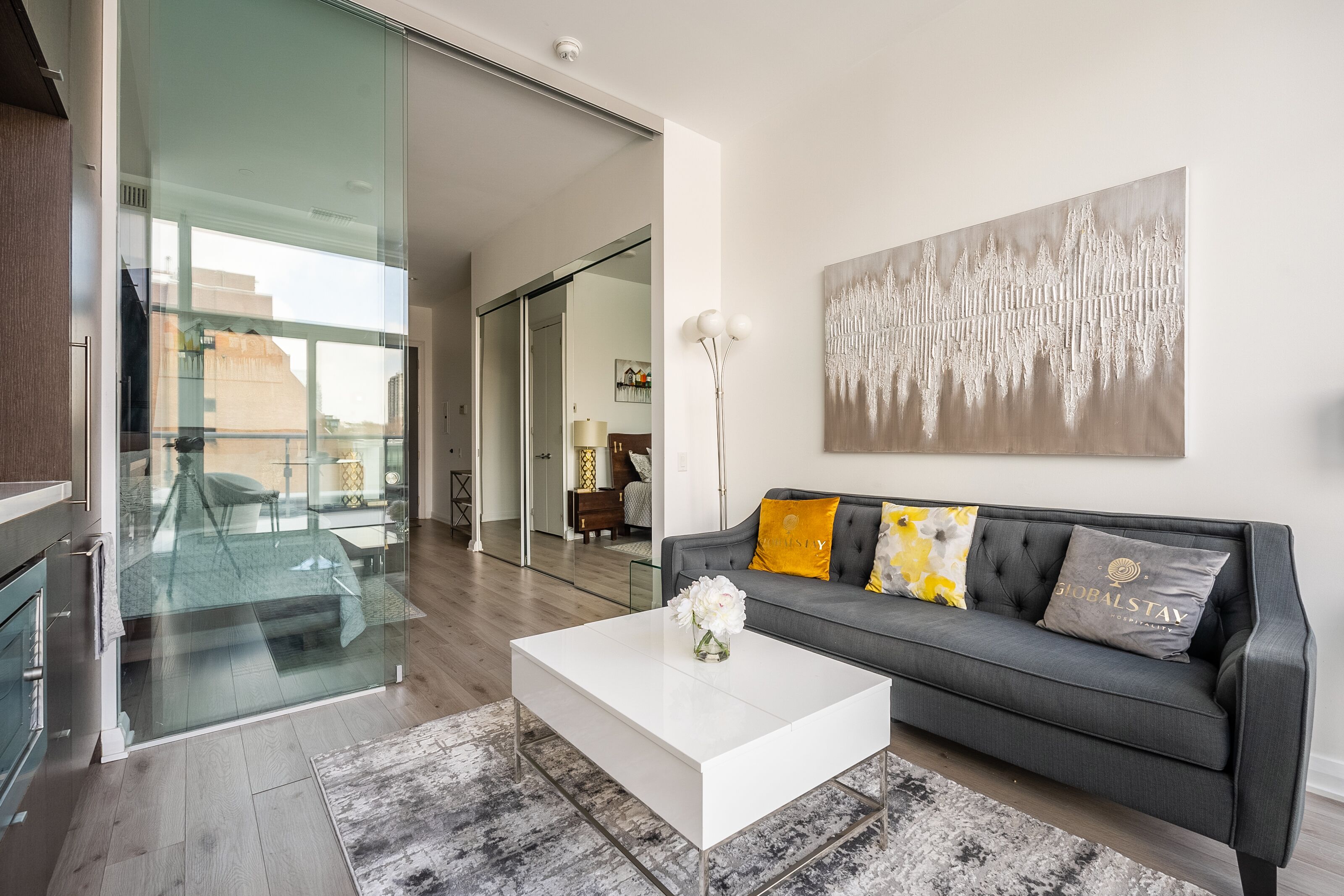 Una sala de estar moderna con un sofá gris, una mesa de centro blanca y un cuadro abstracto grande.