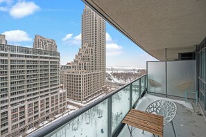 A balcony with a view of tall buildings, a wooden bench, and a glass railing. - Fort York Suites Toronto (Toronto)