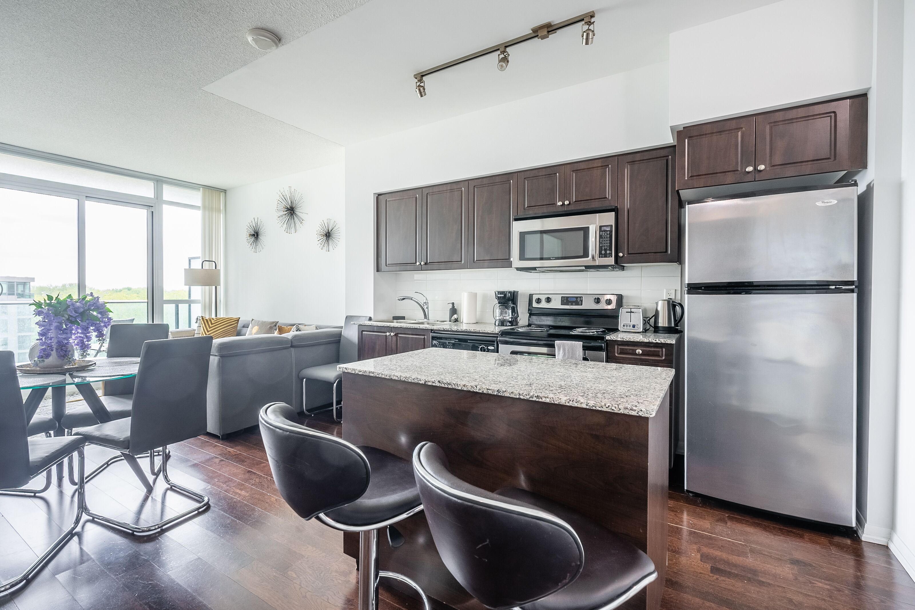 Una cocina moderna con armarios de madera oscura, electrodomésticos de acero inoxidable y una mesa de comedor de vidrio con taburetes de bar.