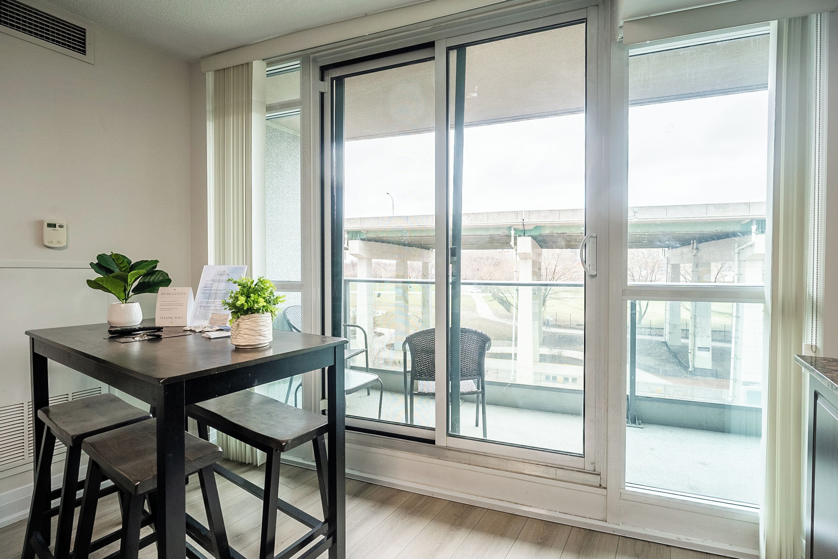 Une chambre moderne dotée d’une grande porte-fenêtre coulissante donnant sur un balcon, d’une petite table avec des chaises et d’une plante en pot.