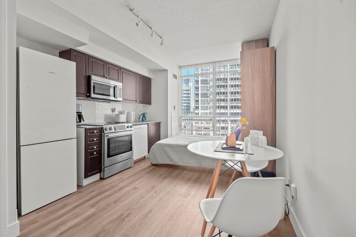 A modern kitchen with white appliances, a dining area with a round table and chairs, and a large window with a city view.