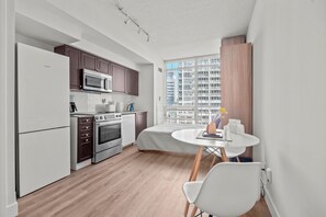 Una cocina moderna con electrodomésticos blancos, un comedor con mesa redonda y sillas, y un amplio ventanal con vistas a la ciudad.