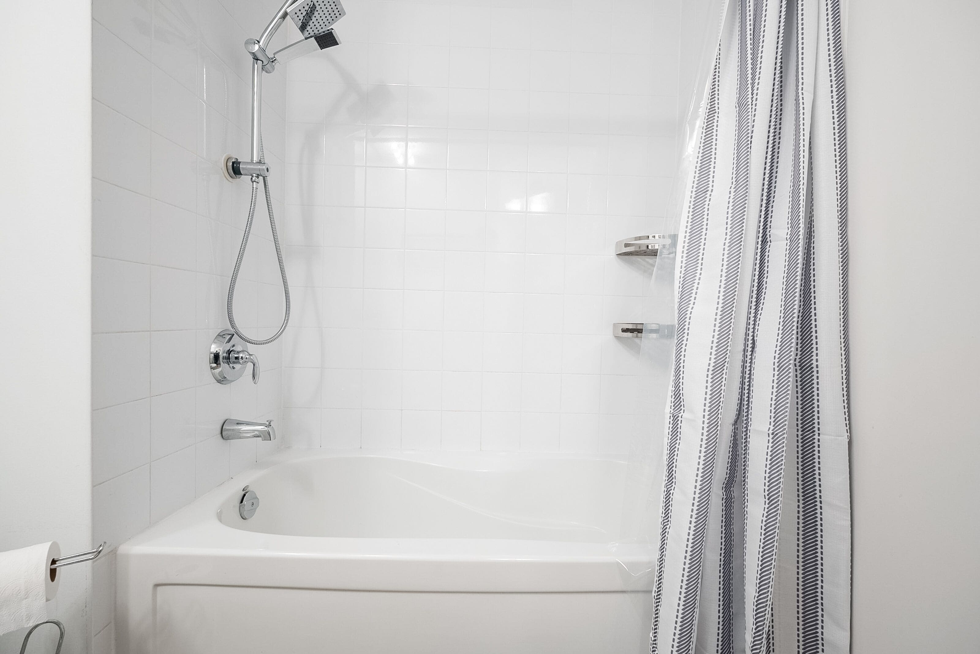 Une salle de bain blanche avec une baignoire, une douche et un rideau de douche à rayures.