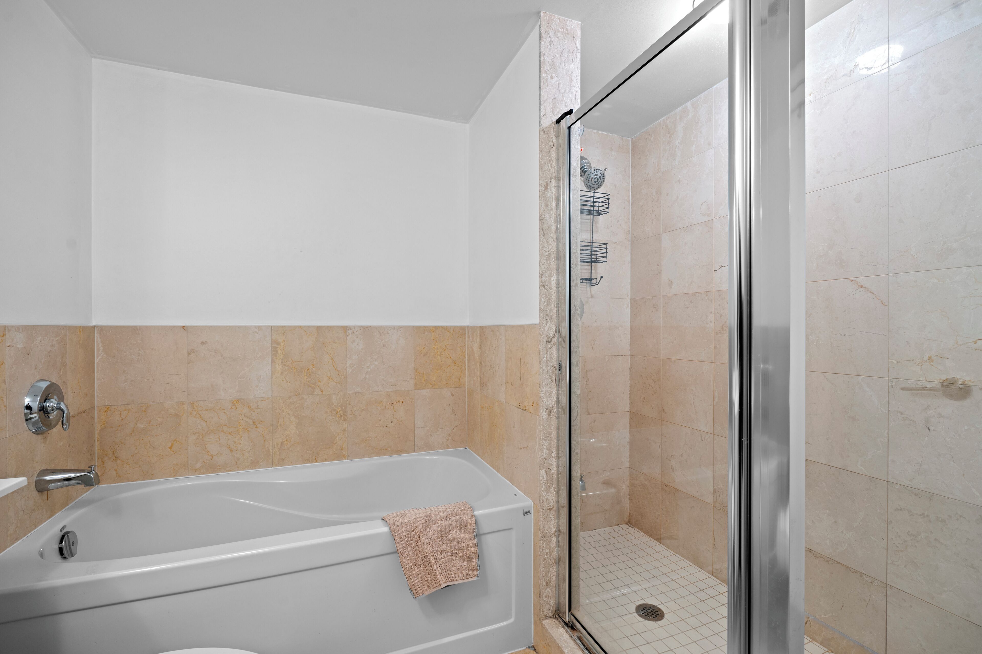 A modern bathroom with a bathtub, a glass shower enclosure, and beige tiled walls.