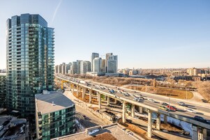 A high-rise building with a modern glass facade, a multi-level highway overpass, and a city skyline in the background.