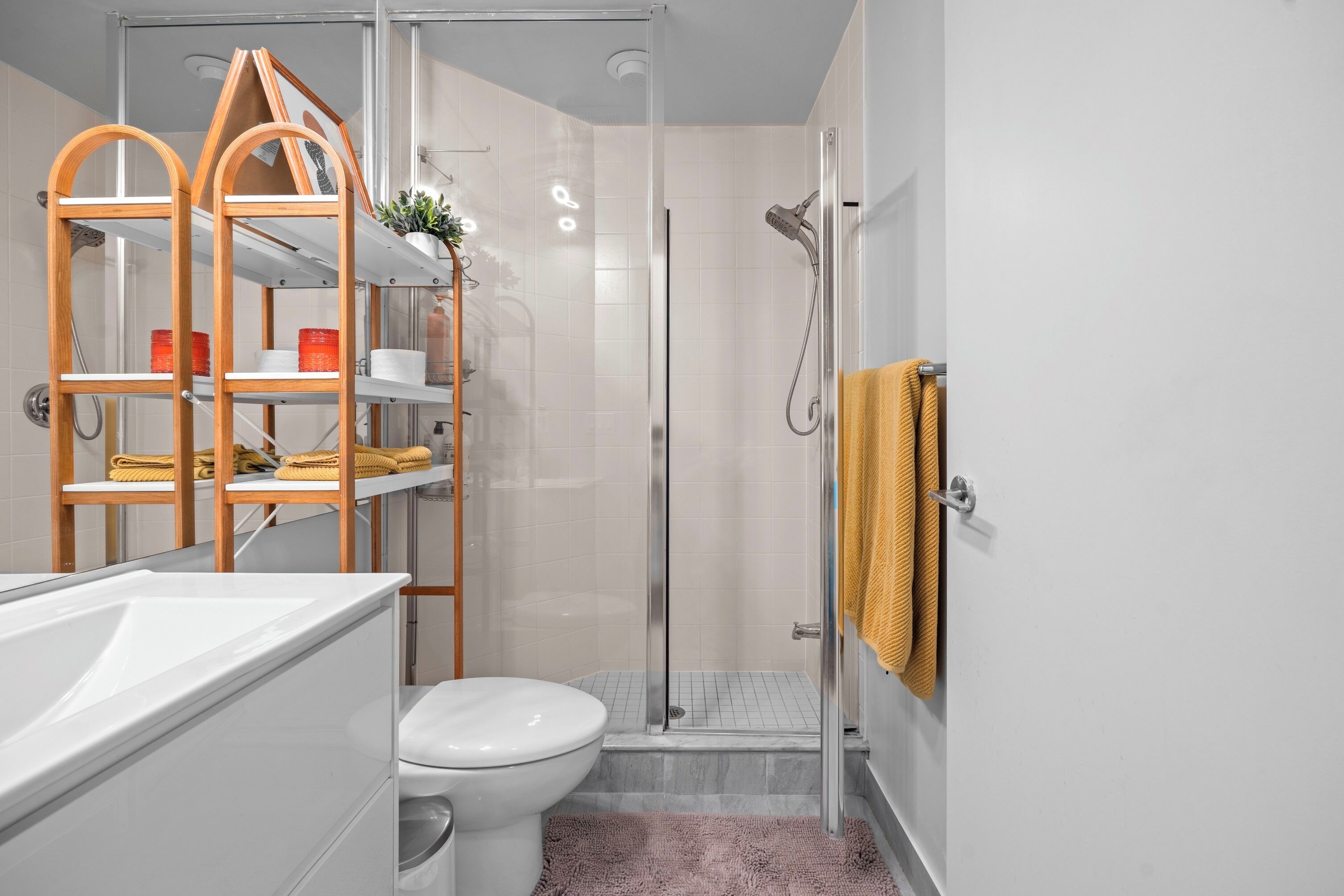 A modern bathroom with a glass shower enclosure, a white toilet, and wooden shelves with toiletries.