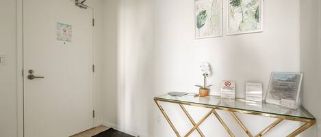 A clean, modern reception area with a glass-top desk, a black doormat, and two framed botanical prints on the wall.