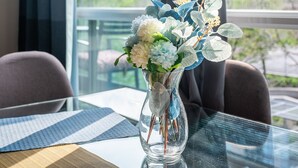 Uma mesa de vidro com um vaso de flores, um jogo americano e vista para a cidade através de uma janela.