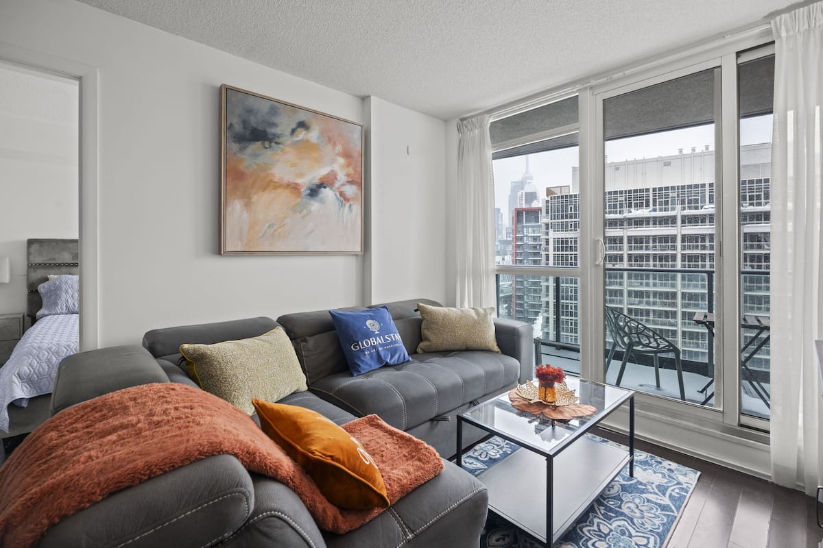 A modern living room with a grey sofa, a coffee table, and a large window with a city view.