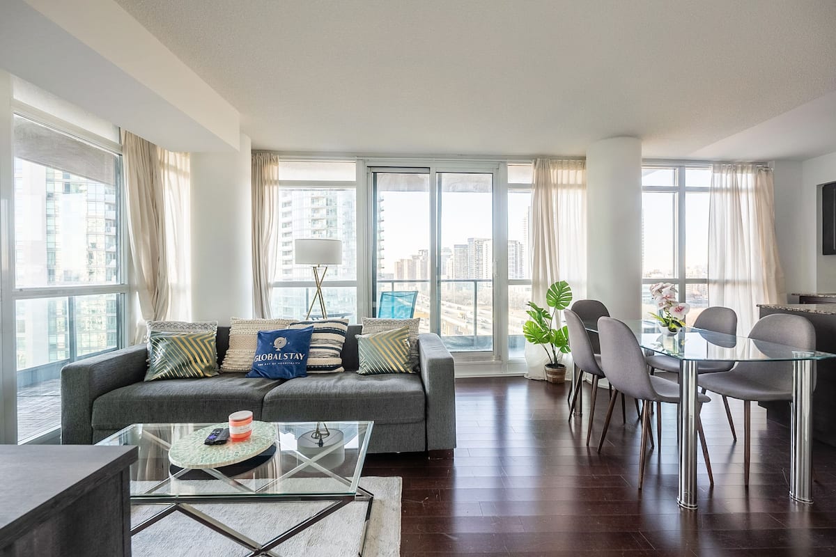 A modern living room with a grey sofa, glass coffee table, and dining area with chairs.