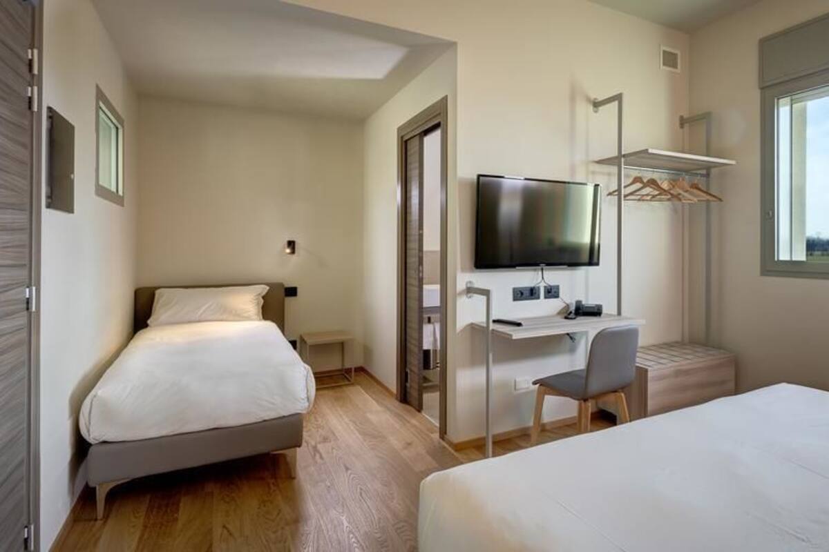 A hotel room with two beds, a desk with a chair, a television, and a window with a view.