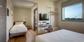 Une chambre d’hôtel avec deux lits, un bureau avec une chaise, une télévision et une fenêtre donnant sur un paysage agréable.