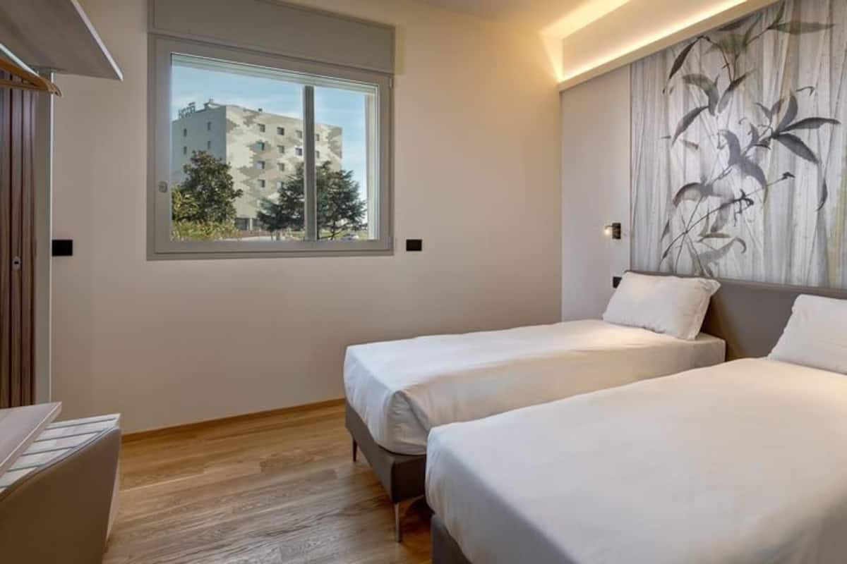 A hotel room with two beds, a large window, and a wall-mounted artwork.