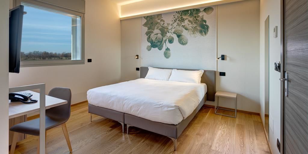 Een moderne slaapkamer met een bed, nachtkastjes, een bureau met stoel, en een raam met uitzicht.