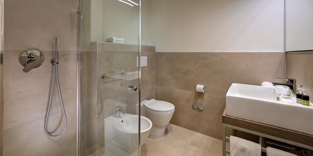Un baño moderno con ducha envuelta en vidrio, inodoro blanco y lavamanos con artículos de aseo.