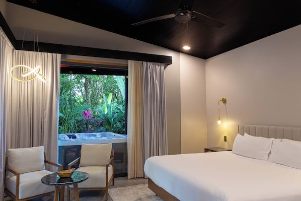 Habitación de hotel moderna con cama, una mesita con sillas, ventilador de techo y vista a zonas verdes.