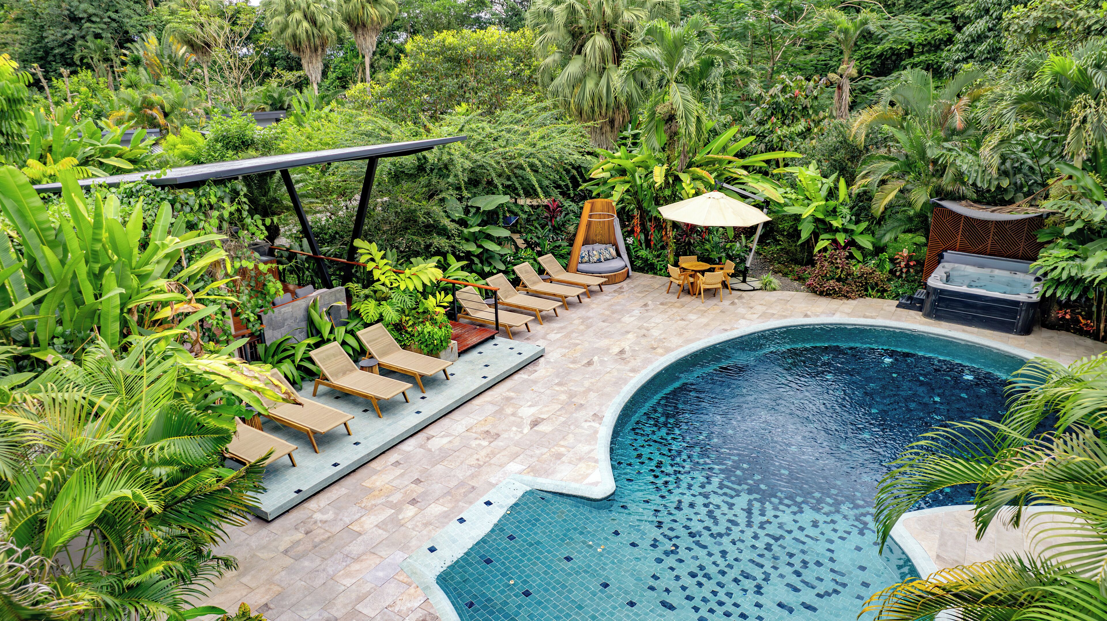 Un área de piscina con sillones reclinables, un jacuzzi y exuberante vegetación.