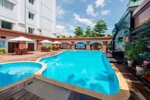 Una piscina con cubierta de madera, sillas de descanso y sombrillas.