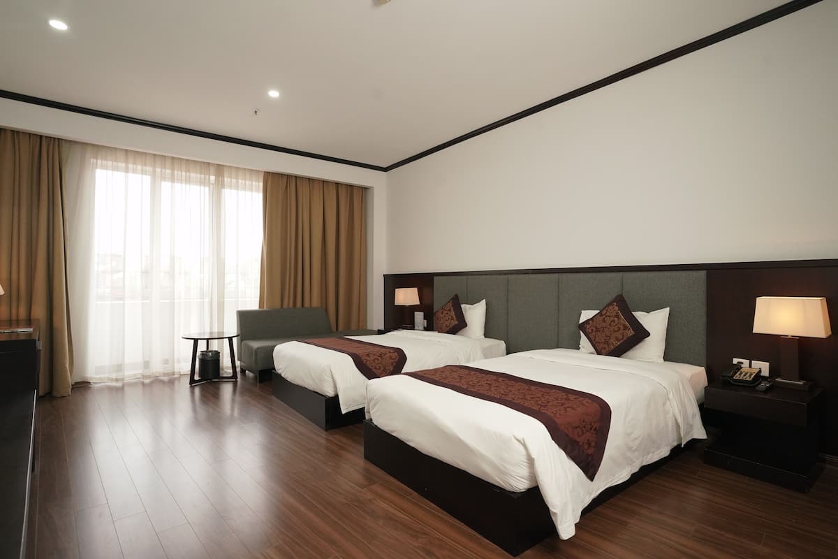 Habitación de hotel con dos camas, un escritorio, una silla y un ventanal con cortinas.