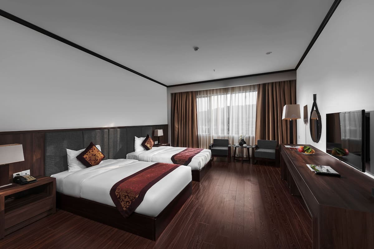 Habitación de hotel con dos camas, un escritorio, una silla, un televisor y una ventana con cortinas.