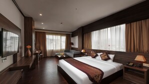 A hotel room with a large bed, a TV, a desk, and a sofa.