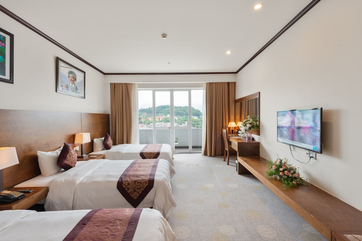 Habitación de hotel con dos camas, un escritorio, un televisor y un ventanal con vistas a la ciudad.