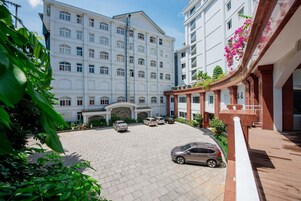 Un hotel de varios pisos con un patio central, varios coches aparcados y abundante vegetación.