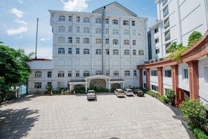 Un edificio de varios pisos con una entrada central, un patio empedrado y varios coches aparcados.