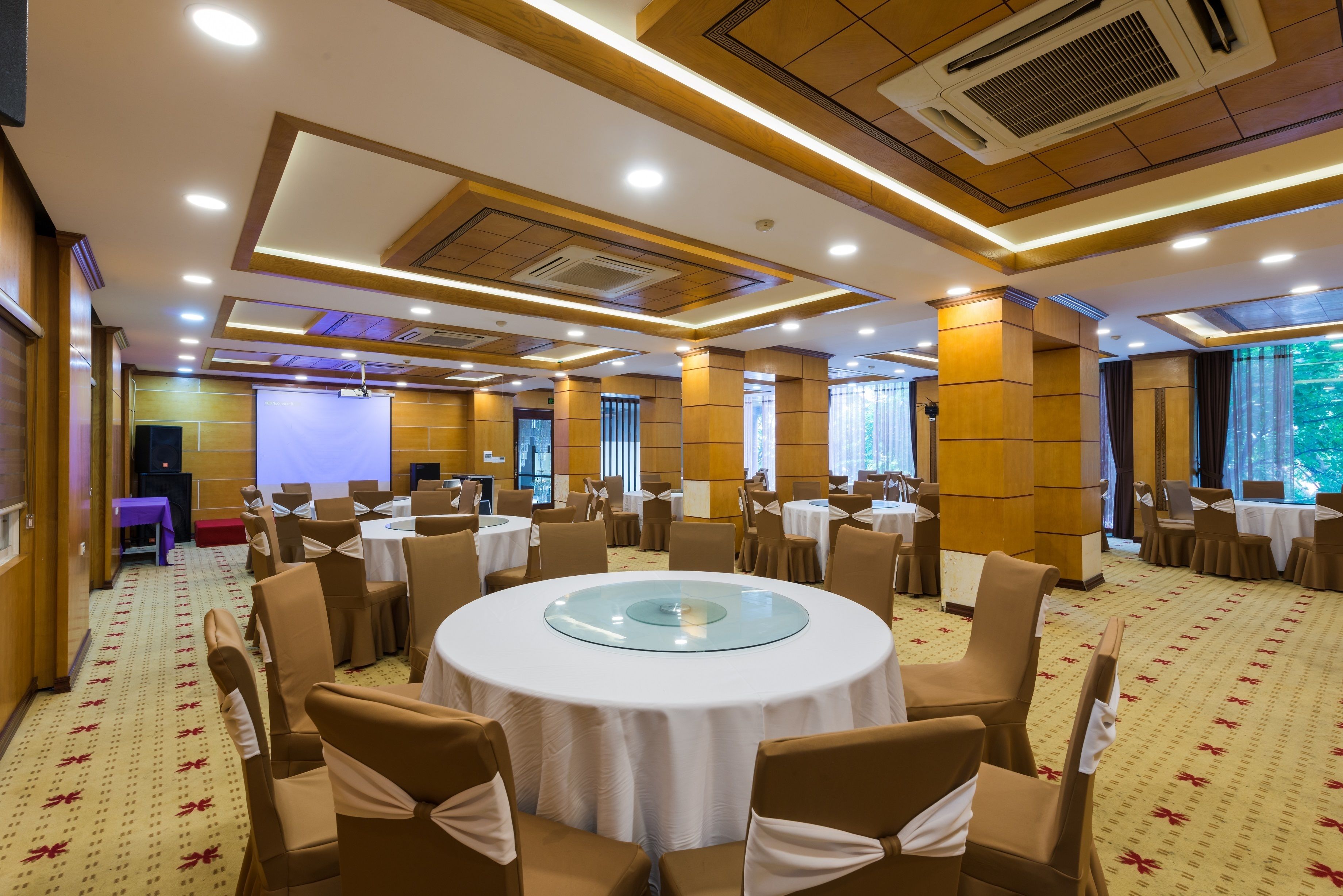 Une salle de conférence équipée de tables rondes, de chaises et d’un grand écran.