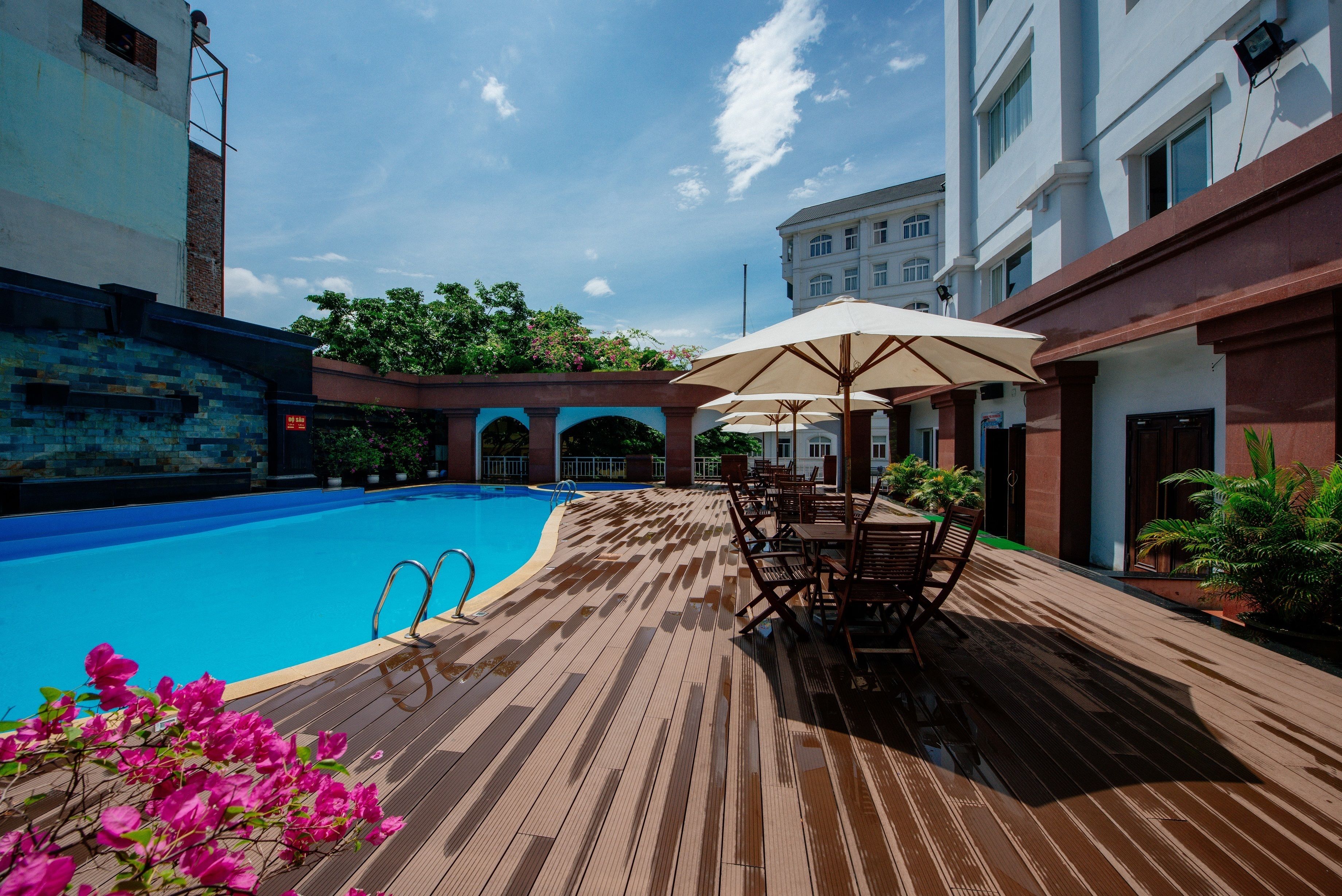 A wooden deck with a pool, outdoor seating, and a building with a balcony.