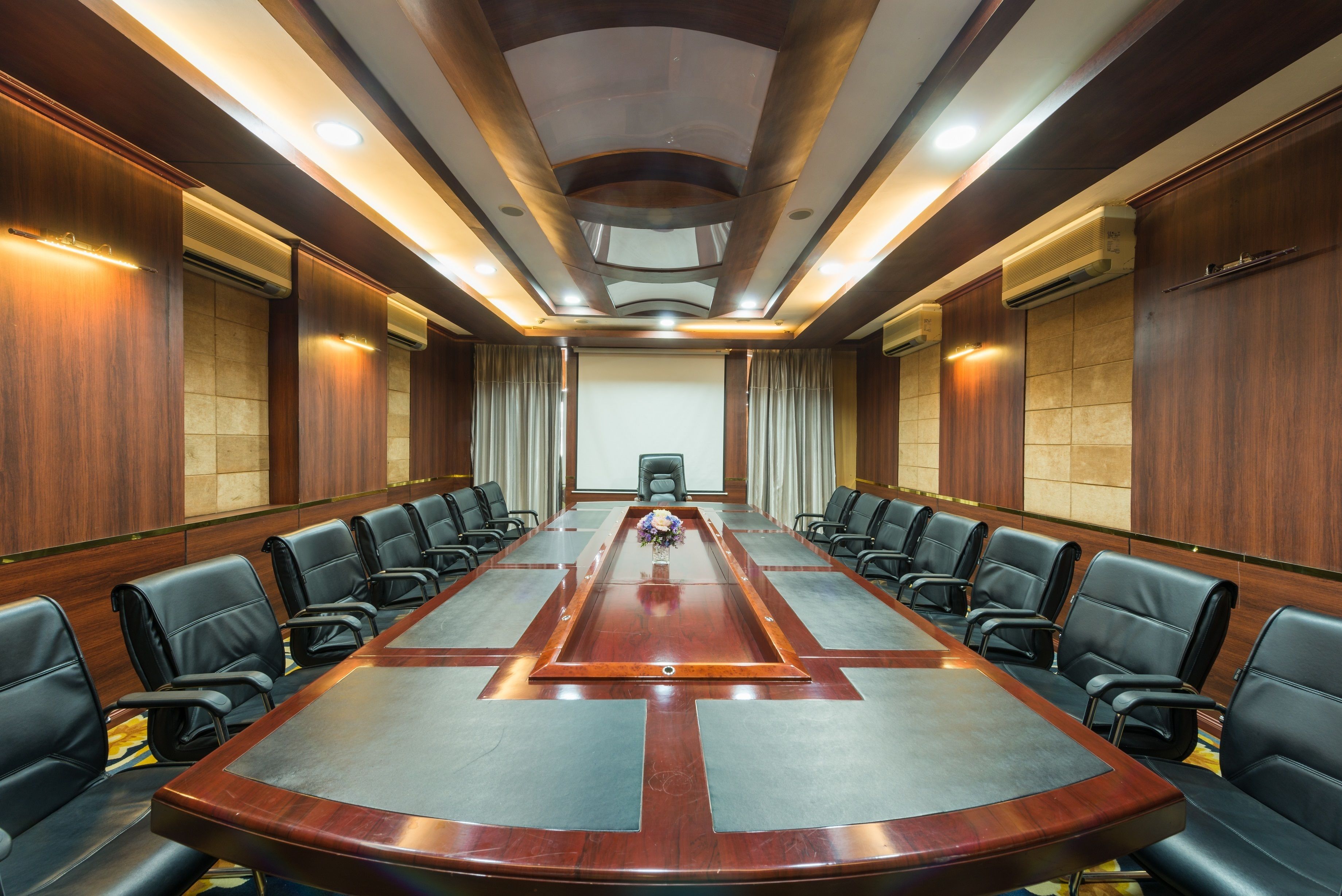 A conference room with a long table, black leather chairs, and wooden paneling.